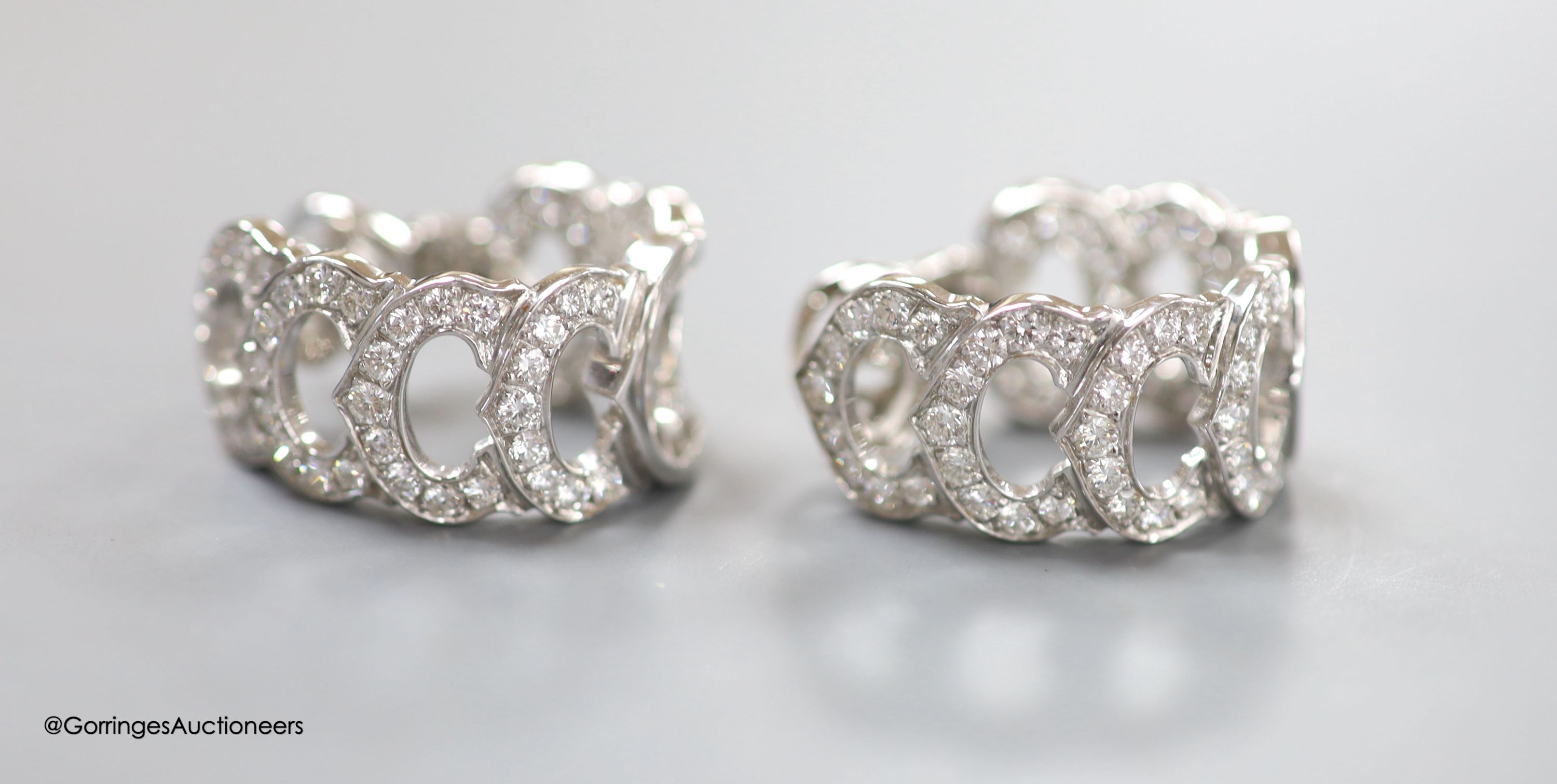 A modern pair of French Cartier white metal (18ct poincon mark) and diamond encrusted '7 C's' earrings, of curved form